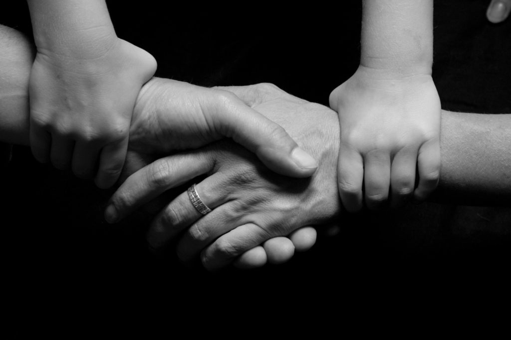 Mother and Father holding hands with child's hands grasping both parents' arms. Adoptive Families