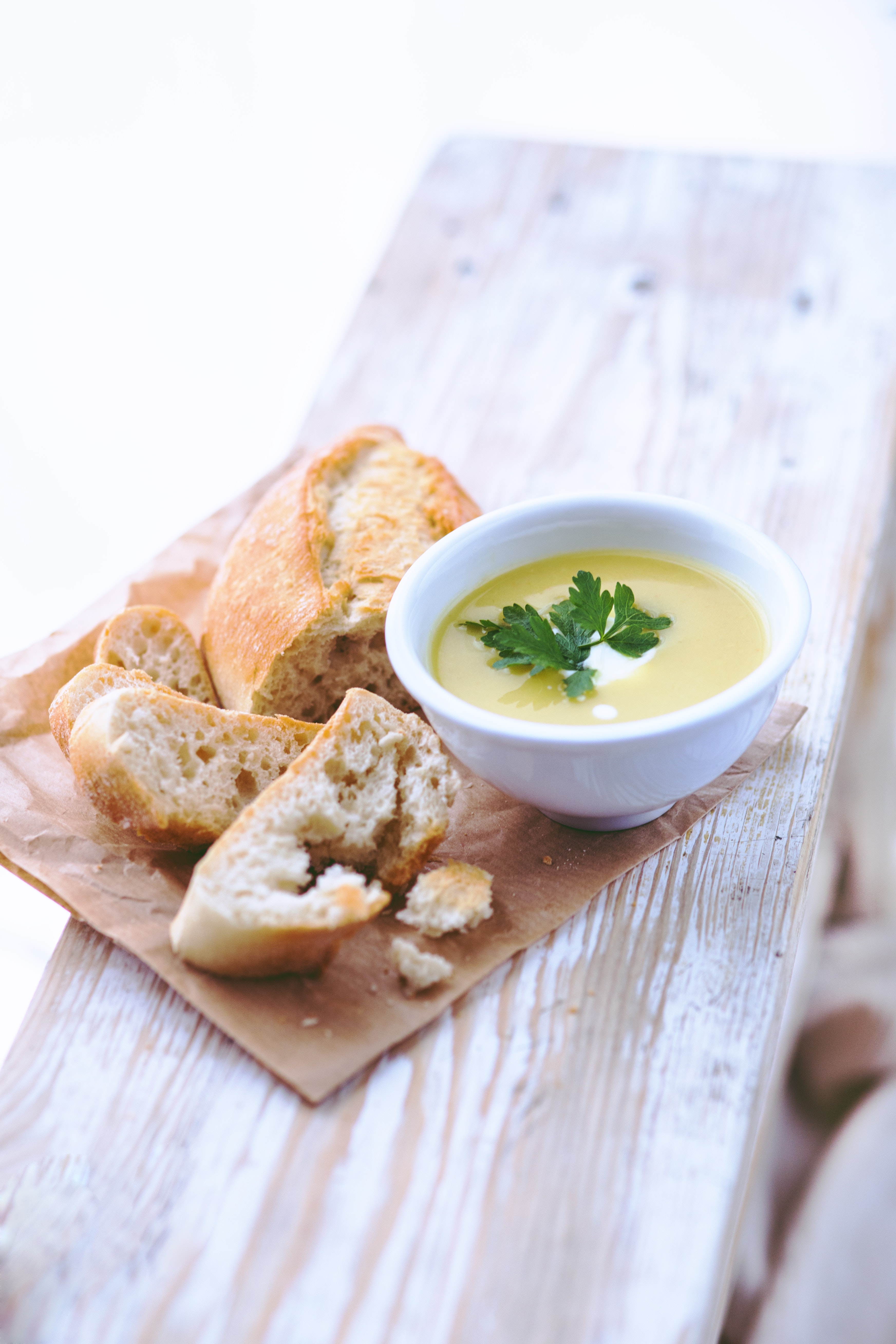 Ceramic bowl with garnished soup next to a sliced baguette on a white wood plank
