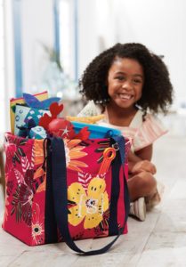 Smiling girl sitting on the floor with her colorful Small Utility Tote full of beach items